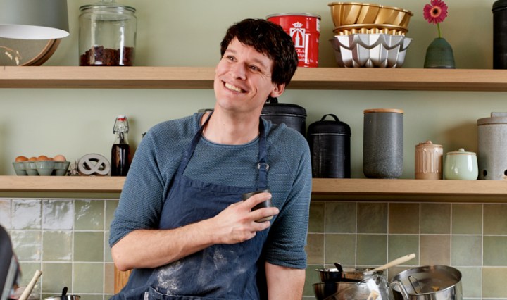 Rutger van den Broek zit op zijn aanrecht. Hij heeft een kopje in zijn hand. Het aanrecht staat vol met vieze bakspullen.